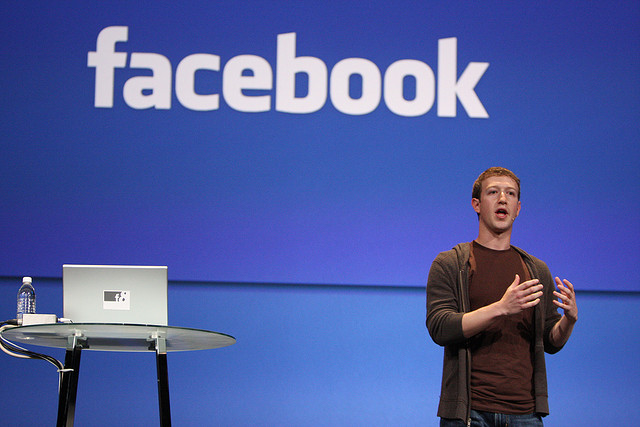 Mark Zuckerberg speaking in front of a large Facebook sign