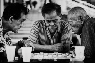 A picture shows three people at a table leaning over a board game.