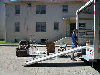 A photo shows a person next to the back of a moving truck unloading furniture.